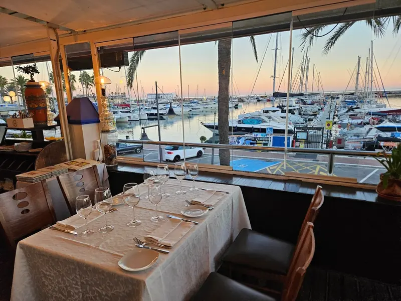 Mesa junto al ventanal con el Puerto Deportivo de Estepona al atardecer