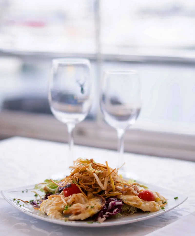 Plato con verduras, tomate cherry y patata paja crujiente junto a la ventana