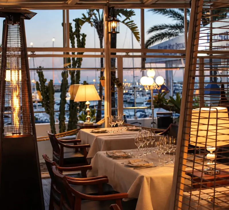 La terraza al anochecer, con lámparas y estufas encendidas frente al puerto
